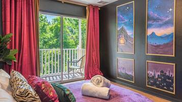 Une chambre avec un balcon, un lit doté de plusieurs oreillers et trois œuvres d’art encadrées accrochées au mur.