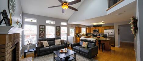 A spacious living area with a fireplace, two sofas, a coffee table, and a ceiling fan.