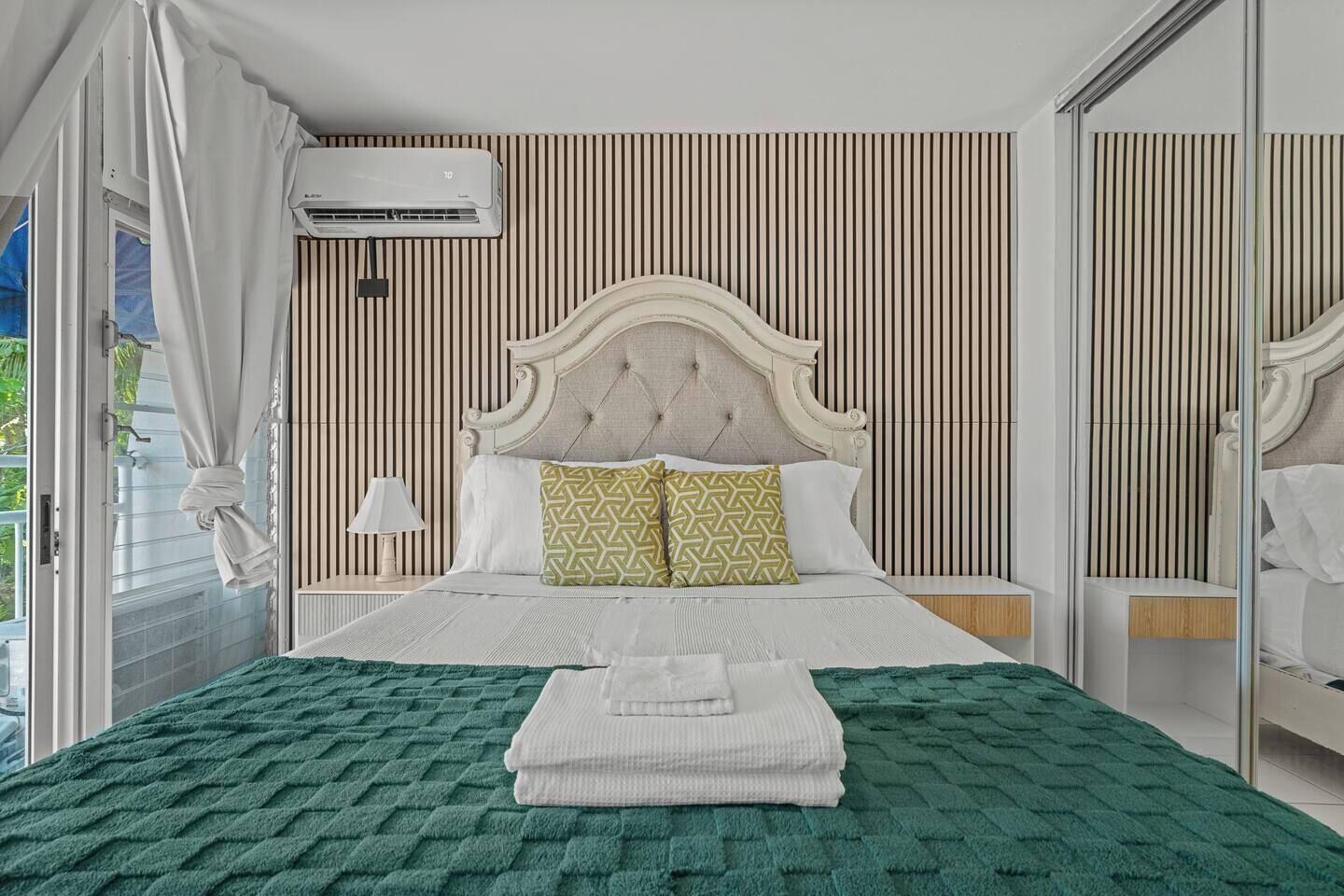 Un dormitorio con cama, lámpara de noche, aire acondicionado y un espejo grande.