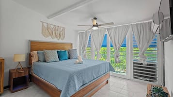 A bedroom with a bed, a nightstand, a ceiling fan, and a view of greenery through the window.