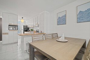 Une cuisine moderne avec des meubles blancs, une table à manger en bois et deux tableaux abstraits accrochés au mur.