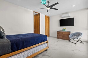 Ein Schlafzimmer mit Bett, Deckenventilator, Fernseher, Kleiderschrank und Stuhl.