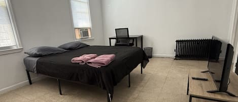 A bedroom with a bed, a desk, a radiator, and a television.