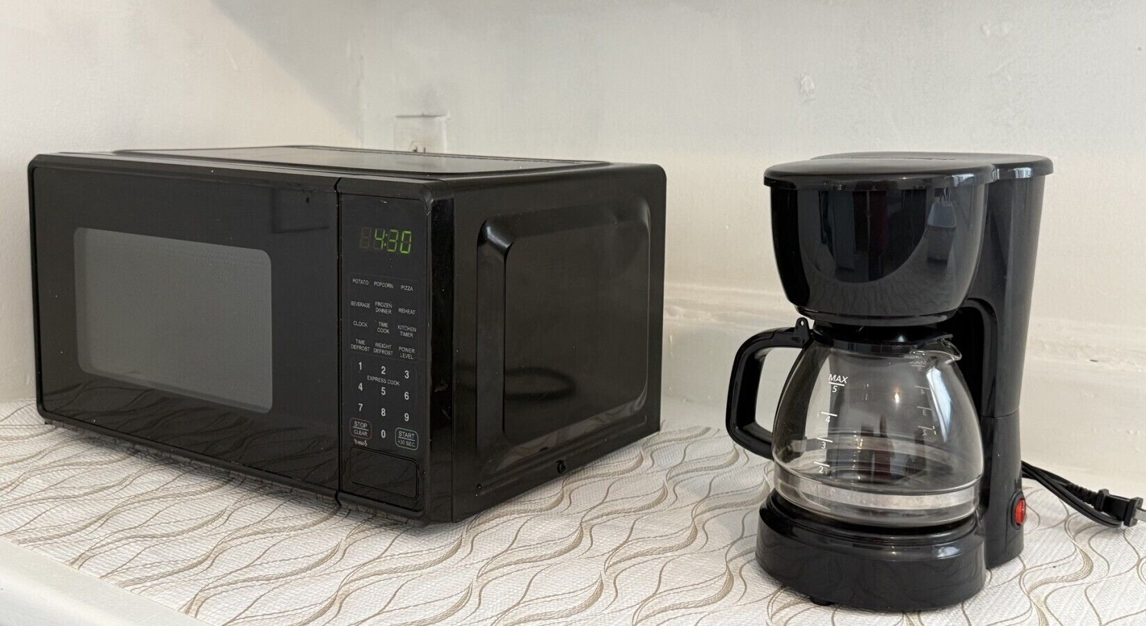 Een zwarte magnetron en een zwarte koffiezetapparaat op een oppervlak met een patroon.