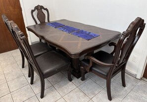 Une table à manger avec quatre chaises, un sol carrelé et une porte visible au fond.