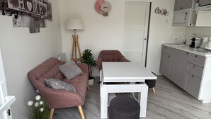 A modern living space with a sofa, a small table, a lamp, and a kitchen area. - Equi Lodge: A Horse-Loving Retreat Near Disney (La Houssaye-en-Brie)