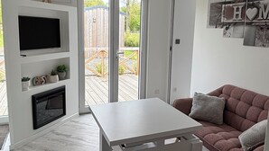 A modern living room with a white TV, a fireplace, a sofa, and a dining table. - Equi Lodge: A Horse-Loving Retreat Near Disney (La Houssaye-en-Brie)
