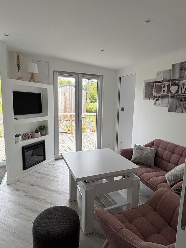 A modern living room with a white TV, a fireplace, a sofa, and a dining table.