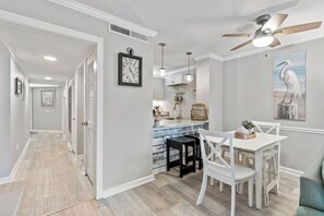A modern kitchen with a built-in island, pendant lighting, and a dining area with white chairs. - Ocean Creek Lodge 4 2276 - Beach, Pools, Hot Tubs (Myrtle Beach)