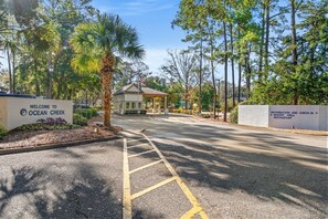 A welcoming sign for Ocean Creek, a paved road leading to a building, and a sign indicating an information and check-in area. - Ocean Creek Lodge 4 2276 - Beach, Pools, Hot Tubs (Myrtle Beach)