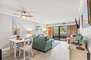 A modern living room with a green sofa, white dining table, and ceiling fan. - Ocean Creek Lodge 4 2276 - Beach, Pools, Hot Tubs (Myrtle Beach)