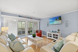A living room with a sofa, a red chair, a coffee table, a TV, and a sliding glass door leading to an outdoor area. - Ocean Creek Lodge 1 2422 - Beach, Pools, Hot Tubs (Myrtle Beach)
