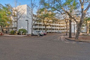A multi-story building with a parking lot and trees. - Ocean Creek Lodge 1 2422 - Beach, Pools, Hot Tubs (Myrtle Beach)