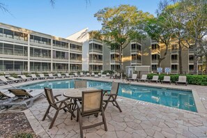 A swimming pool with lounge chairs and a table, surrounded by a building with multiple balconies. - Ocean Creek Lodge 1 2422 - Beach, Pools, Hot Tubs (Myrtle Beach)
