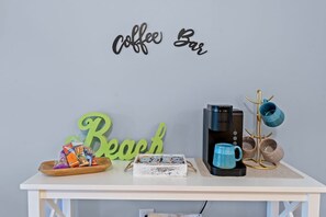 A coffee bar setup with a coffee maker, mugs, and a tray of snacks. - Ocean Creek Lodge 1 2422 - Beach, Pools, Hot Tubs (Myrtle Beach)