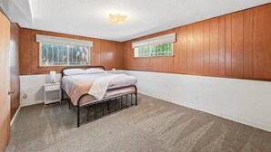 Ein Schlafzimmer mit einem Bett, einem Nachttisch und zwei Fenstern mit Jalousien.