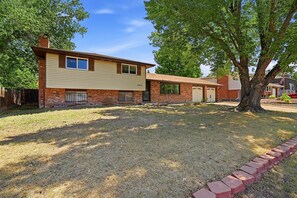 A two-story house with a brick facade, a front yard with a tree, and a clear sky. - Peaceful 4-bedroom house with AC in Colorado Springs (Colorado Springs)