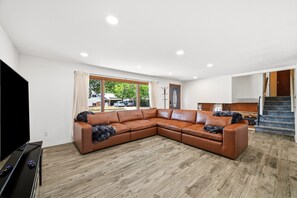A modern living room with a sectional sofa, a flat-screen TV, and a staircase leading to an upper level. - Peaceful 4-bedroom house with AC in Colorado Springs (Colorado Springs)