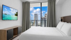 Ein Hotelzimmer mit Bett, Fernseher an der Wand und Blick auf Stadt und Meer.