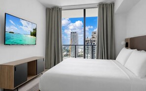 Ein Hotelzimmer mit Bett, Fernseher an der Wand und Blick auf Stadt und Meer.