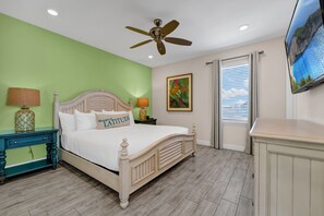 Une chambre à coucher avec un lit, un ventilateur de plafond, une télévision, une fenêtre avec des stores et un mur vert.
