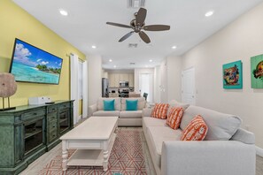 A living room with a sofa, coffee table, and a television on a wall. - Tropical Cottage near Disney with Margaritaville Resort and Island H20. (Kissimmee)