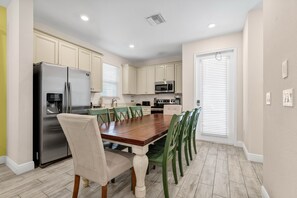 A modern kitchen with a dining area, featuring a stainless steel refrigerator, a microwave, and a wooden dining table with chairs. - Tropical Cottage near Disney with Margaritaville Resort and Island H20. (Kissimmee)