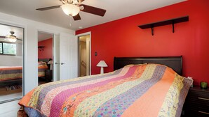 Ein Schlafzimmer mit einem Bett, einem Deckenventilator, einem Nachttisch und einer roten Wand.