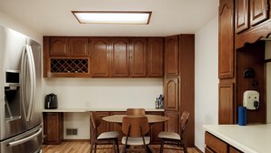 A kitchen with wooden cabinets, a stainless steel refrigerator, a round dining table with chairs, and a built-in wine cooler.