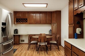 A kitchen with wooden cabinets, a stainless steel refrigerator, a round dining table with chairs, and a built-in wine cooler.