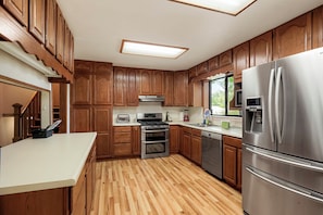 A kitchen with wooden cabinets, stainless steel appliances, and a wooden floor.