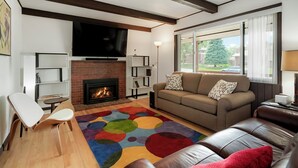 Ein Wohnzimmer mit Kamin, einer Couch, einem Fernseher und einem farbenfrohen Teppich.