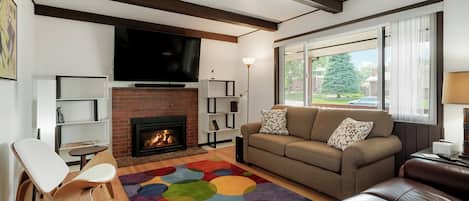 A living room with a fireplace, a sofa, a TV, and a colorful rug.