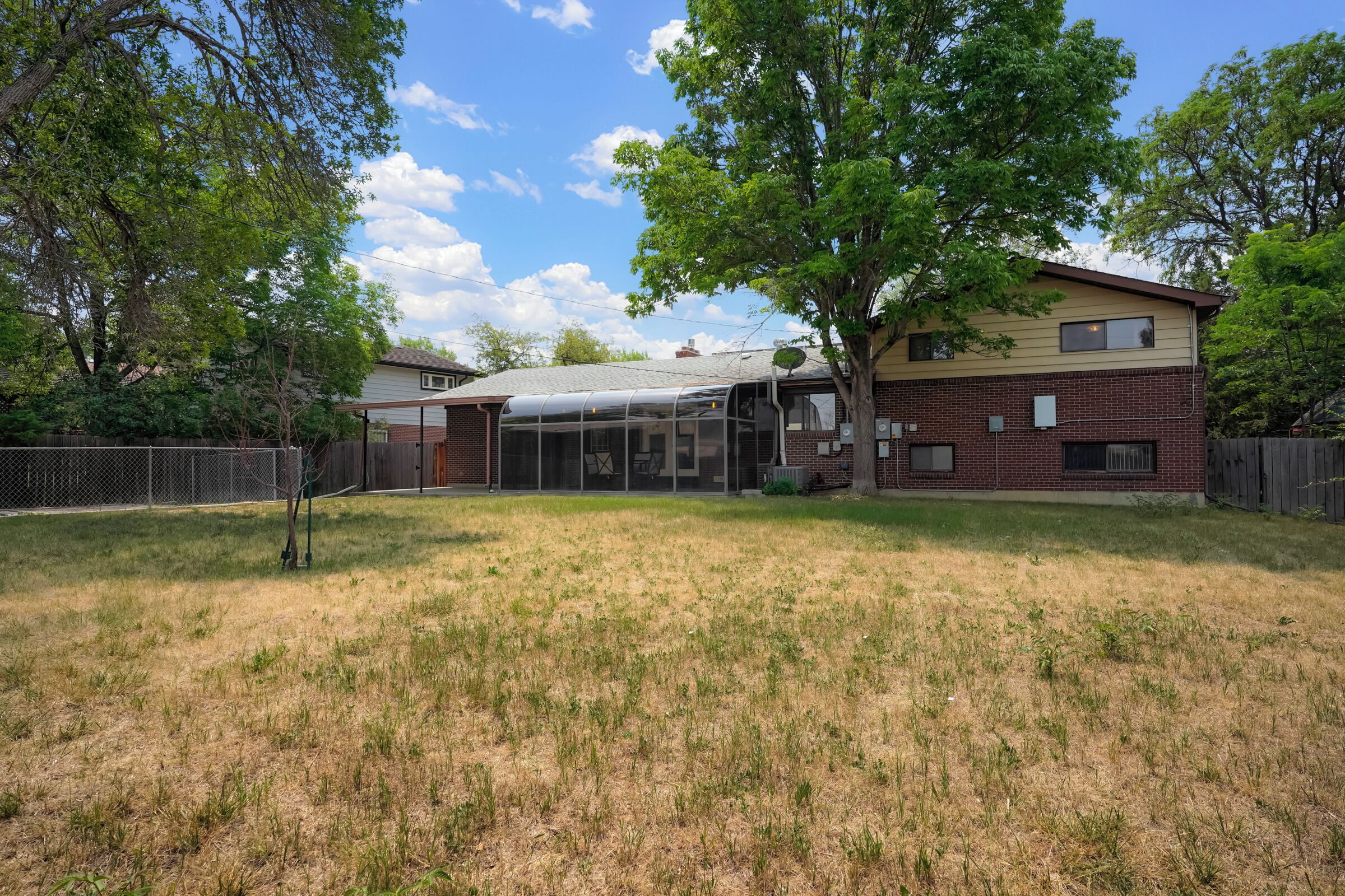 A two-story house with a covered patio, a fenced yard, and mature trees.