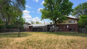 A two-story house with a covered patio, a fenced yard, and mature trees.