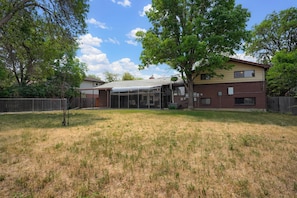 A two-story house with a covered patio, a fenced yard, and mature trees.