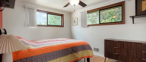 Ein Schlafzimmer mit einem Bett, einem Deckenventilator, einer Kommode und zwei Fenstern.