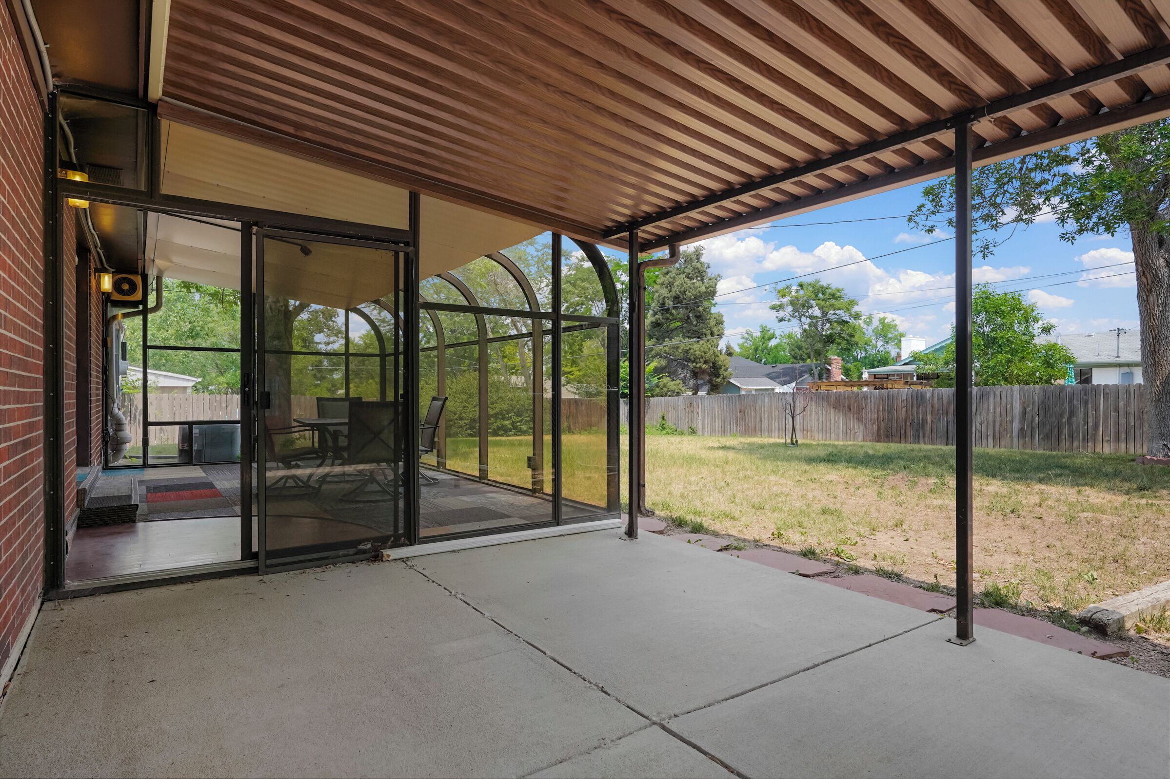 A covered patio with a glass door leading to an outdoor seating area.