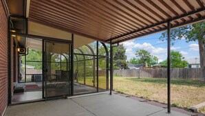 A covered patio with a glass door leading to an outdoor seating area.