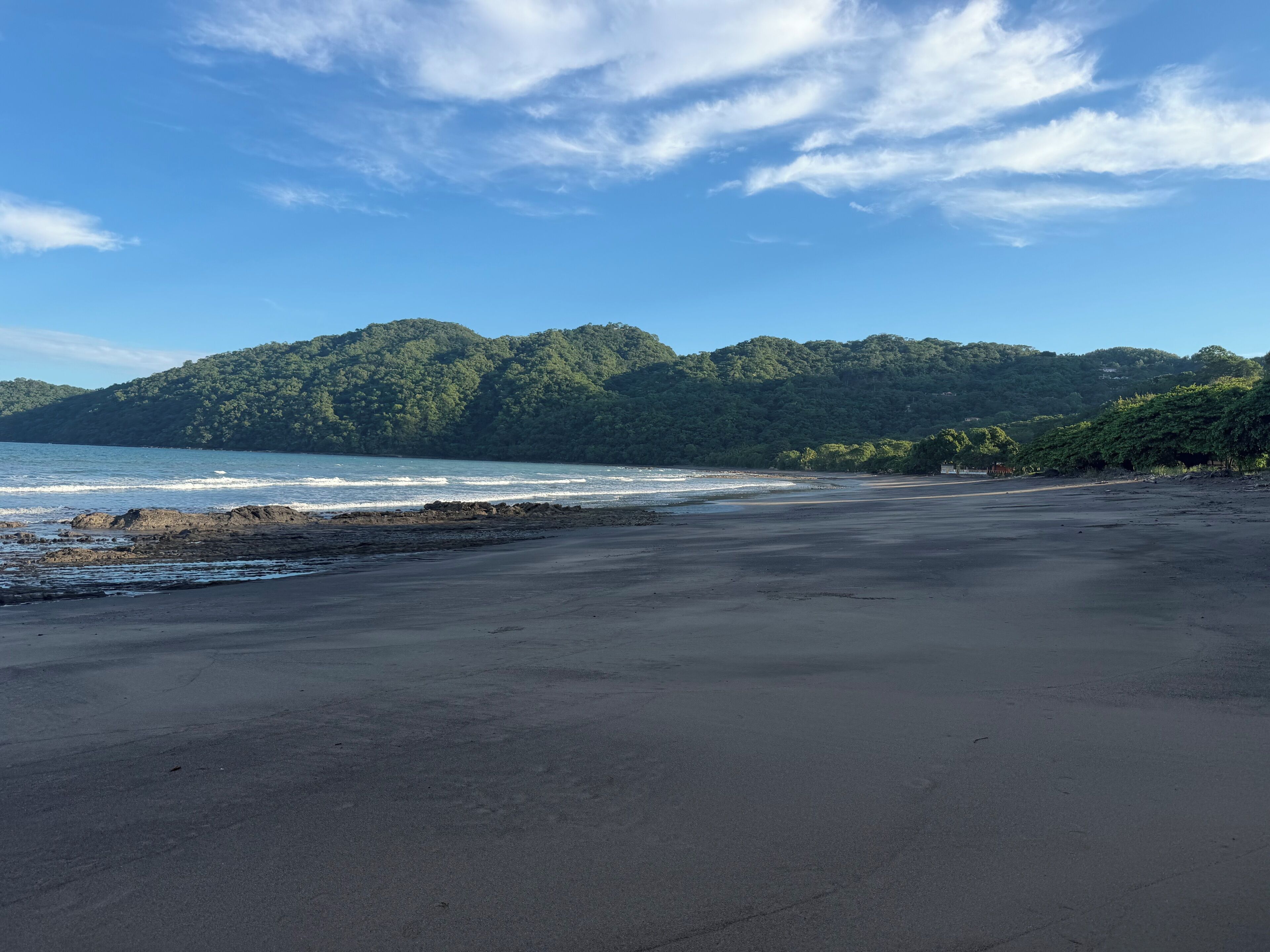 A beach with a rocky shoreline and a forested hill in the background.
