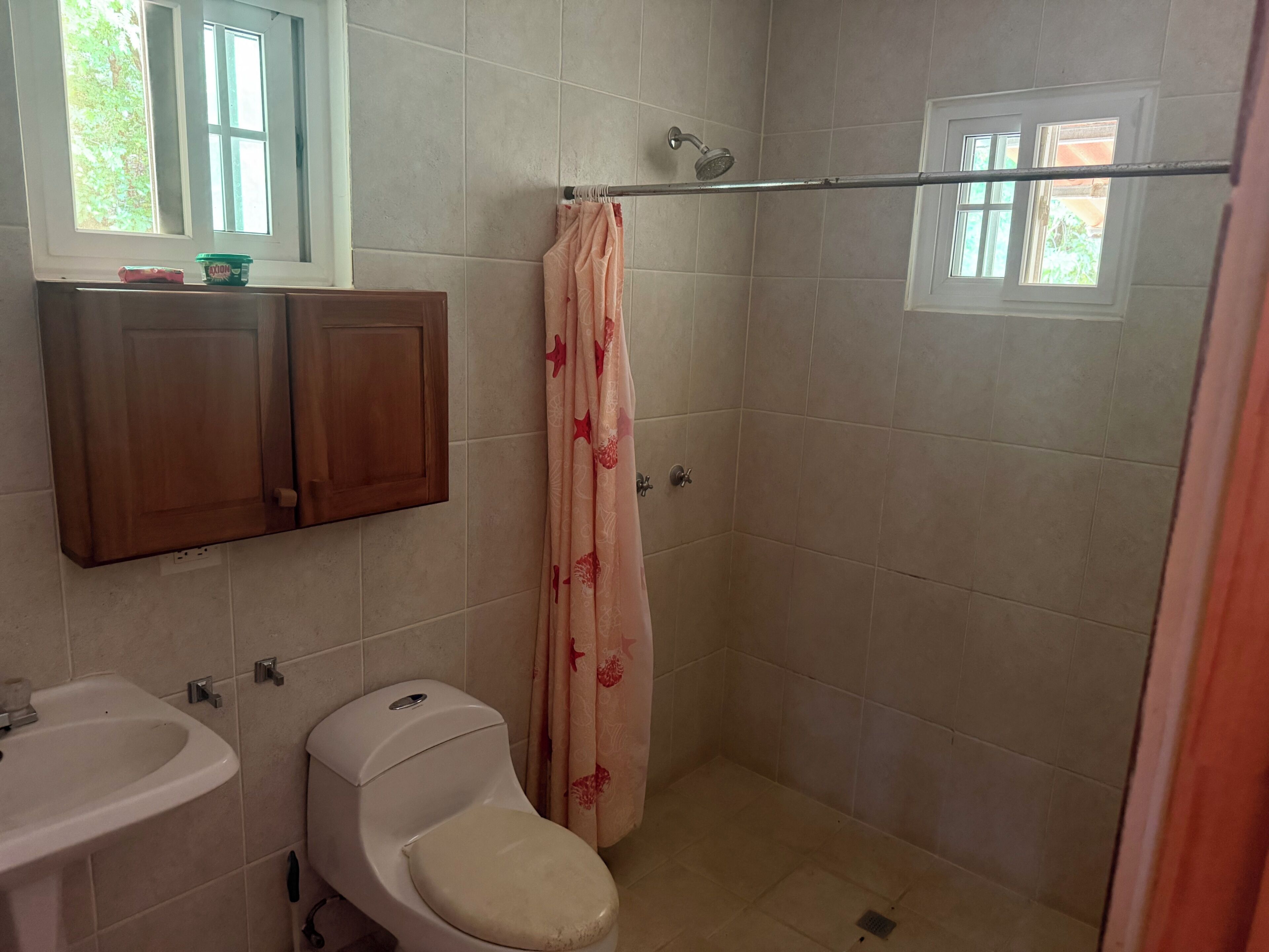 Un baño con inodoro, lavabo, ducha y armarios de madera.