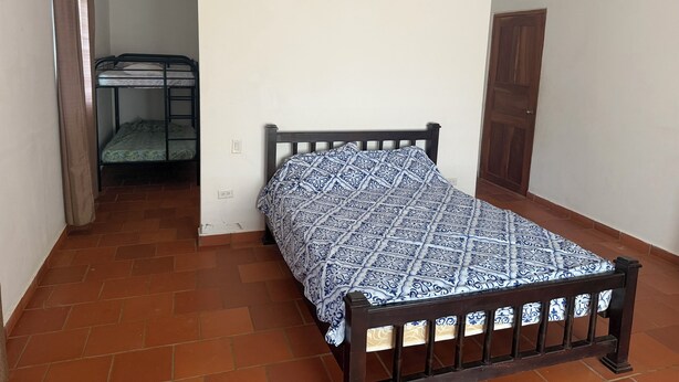 A single bed with a patterned bedspread in a room with a tiled floor and a wooden door. - Ocean view, with pool ,block to beach , , Cozy 1-room house in bucaro with AC (Tonosí)