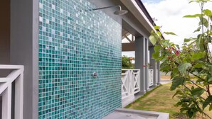A covered outdoor area with a tiled wall, a showerhead, and a plant with red flowers. - DraxHall~3BR~Poo ~Beach Access - 24hr Security (St. Ann's Bay)