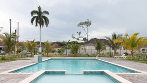 A rectangular swimming pool with a tiled edge, surrounded by palm trees and a paved walkway. - DraxHall~3BR~Poo ~Beach Access - 24hr Security (St. Ann's Bay)