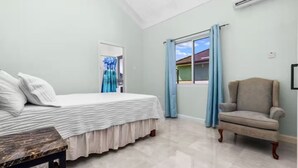 A bedroom with a bed, a chair, a window with curtains, and an air conditioning unit. - DraxHall~3BR~Poo ~Beach Access - 24hr Security (St. Ann's Bay)