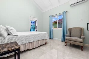 A bedroom with a bed, a chair, a window with curtains, and an air conditioning unit.