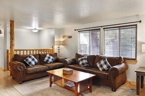 A living room with two brown leather sofas, a wooden coffee table, and a window with blinds. - Mountain Getaway • Hot Tub • Game Room • Sleeps 10 • Minutes to Payette Lake (McCall)