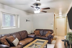 A living room with a brown leather sofa, a glass coffee table, a ceiling fan, and a door in the background. - Mountain Getaway • Hot Tub • Game Room • Sleeps 10 • Minutes to Payette Lake (McCall)