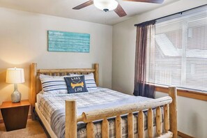 A bedroom with a wooden bed, a ceiling fan, a window with blinds, and a wall-mounted sign. - Mountain Getaway • Hot Tub • Game Room • Sleeps 10 • Minutes to Payette Lake (McCall)