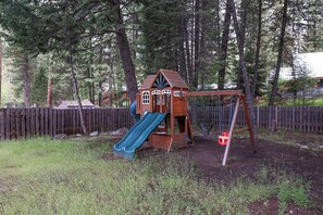 A wooden playhouse with a slide and swing set in a wooded area. - Mountain Getaway • Hot Tub • Game Room • Sleeps 10 • Minutes to Payette Lake (McCall)